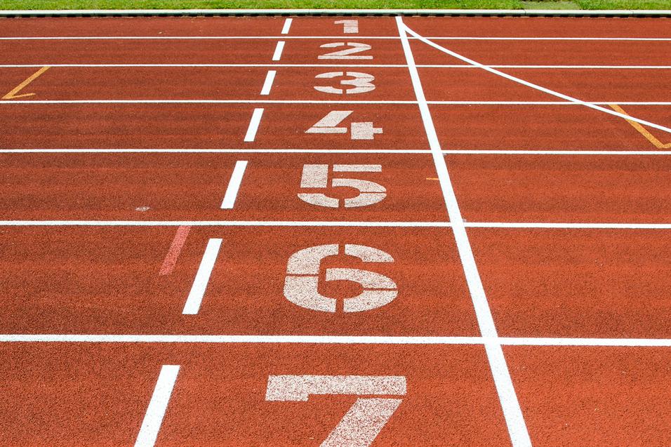 Nahaufnahme einer roten Laufbahn mit den Startnummern 1 bis 8 und grünem Rasen im Hintergrund.